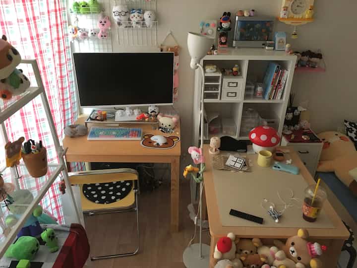 ホワイトの壁とブラウンの木製デスクがあるコンパクトなホームオフィス、キャラクター雑貨とぬいぐるみが印象的な空間