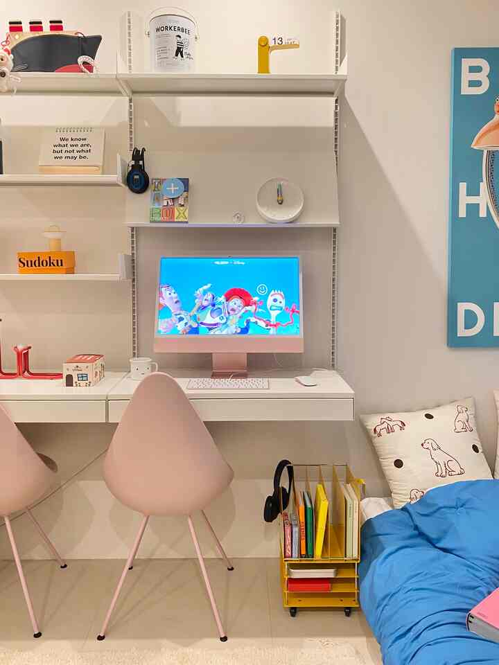 ホワイトとイエローのトーンのコンパクトなホームオフィス空間、デスクと本棚、イエロートロリー、ブルーのベッドリネンが配置された雰囲気のあるインテリア