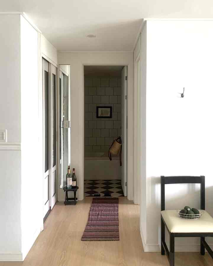 白と木目調の細い廊下、ダイニングチェアと浴室が見えるミニマルな雰囲気のあるインテリア