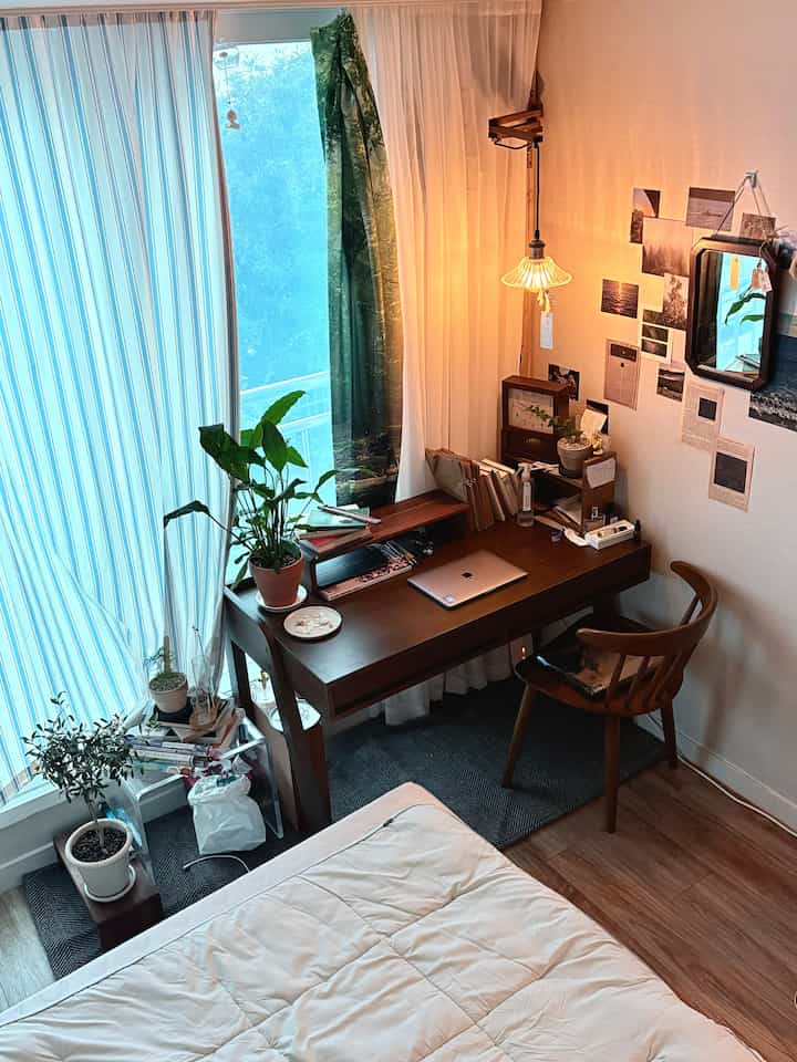 ナチュラルな木目調のワンルーム寝室とホームオフィス空間、木製のデスクとベッド、暖かい照明と植物が配置された雰囲気のあるインテリア