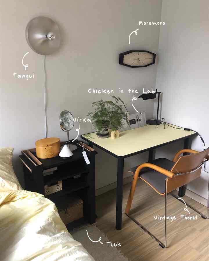 ホワイトの壁とベージュのデスク天板があるナチュラルトーンのワークスペース、ヴィンテージチェアと黒い棚が配置されている印象的な空間