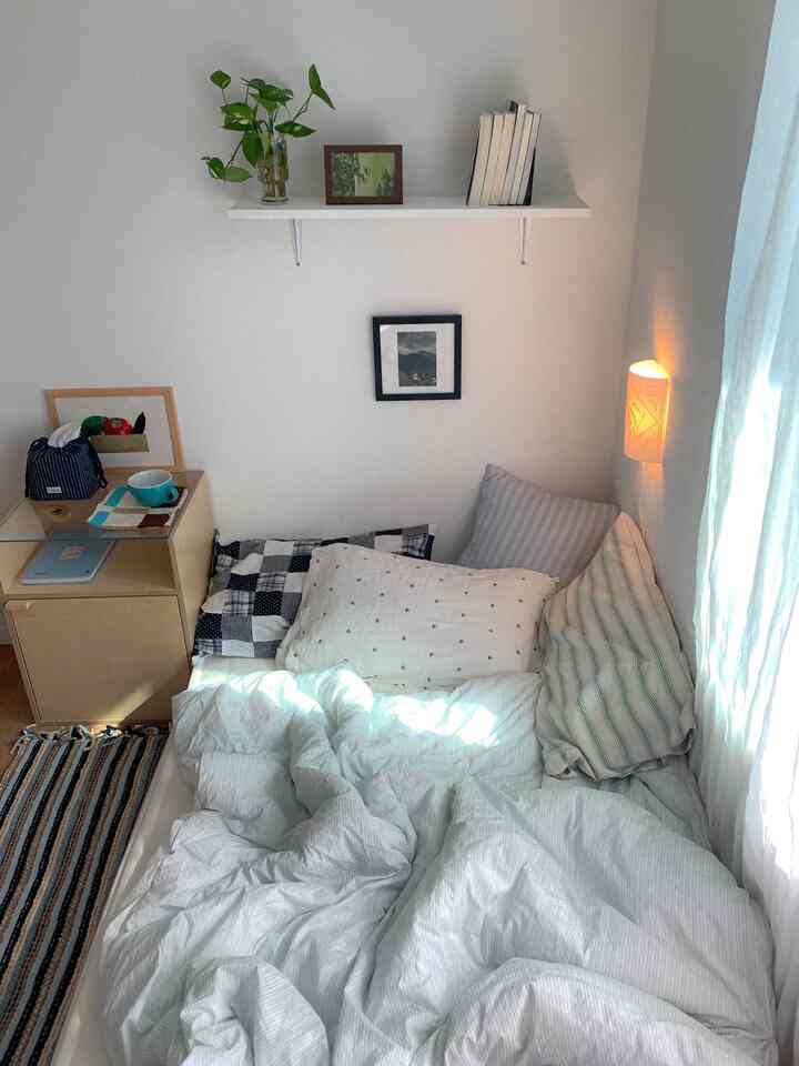 白と木目調が調和した一人用の小さな寝室、壁棚と心地よい寝具が配置された雰囲気のあるインテリア