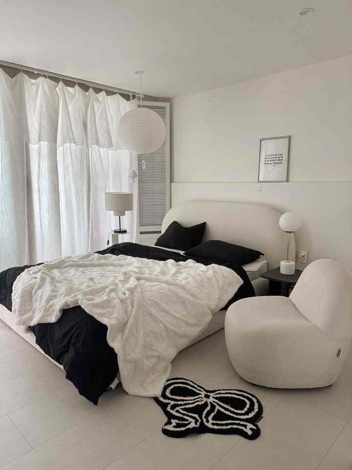 白と黒のモノトーンの寝室、柔らかい寝具とアームチェアが配置されたシンプルモダンな印象的な空間