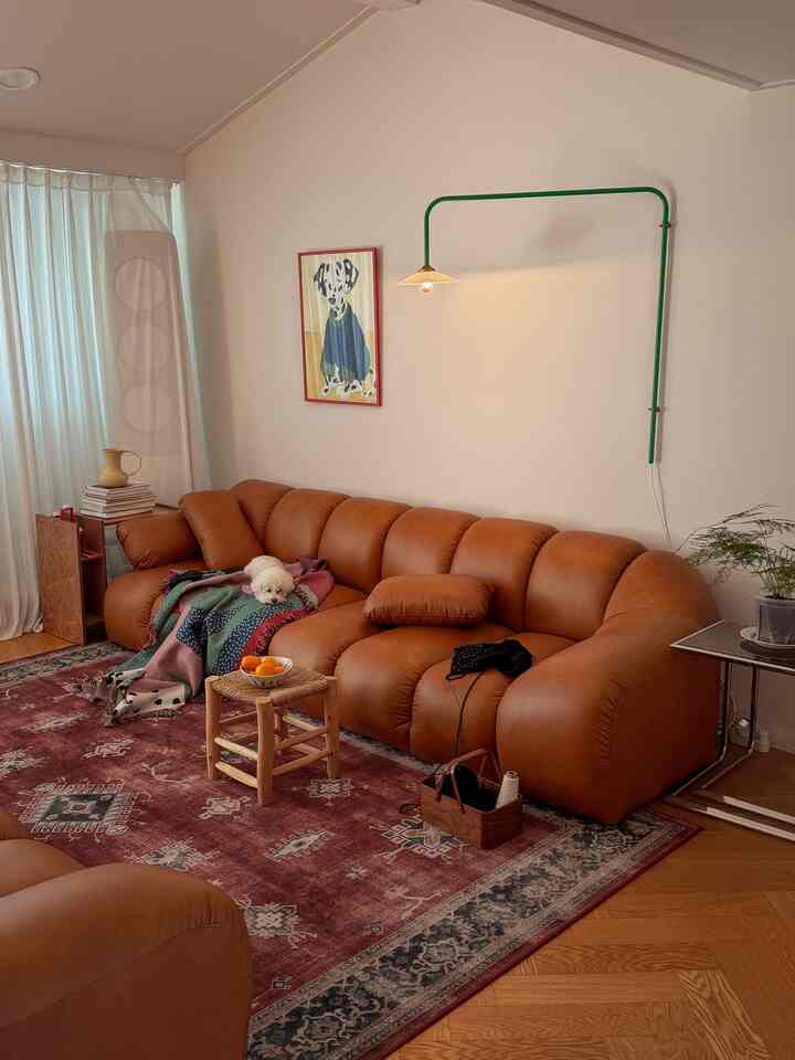 温かみのあるブラウンとナチュラルトーンのリビング、広いレザーソファとラグ、壁掛け照明が配置された雰囲気のあるインテリア