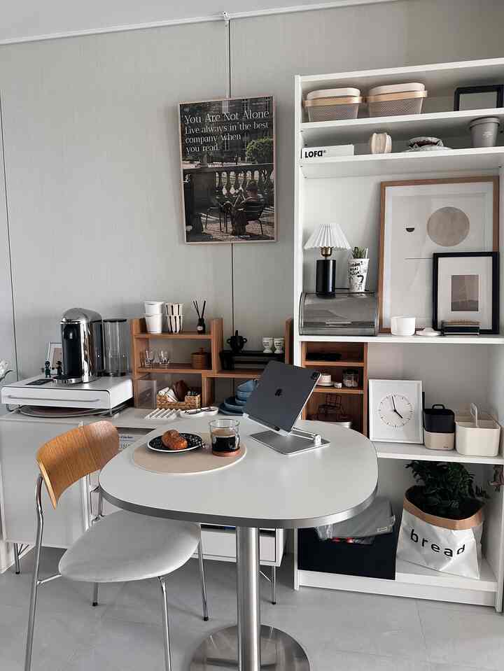 白と茶色のトーンのコンパクトなホームカフェ空間、丸テーブルと本棚が配置された印象的なインテリア