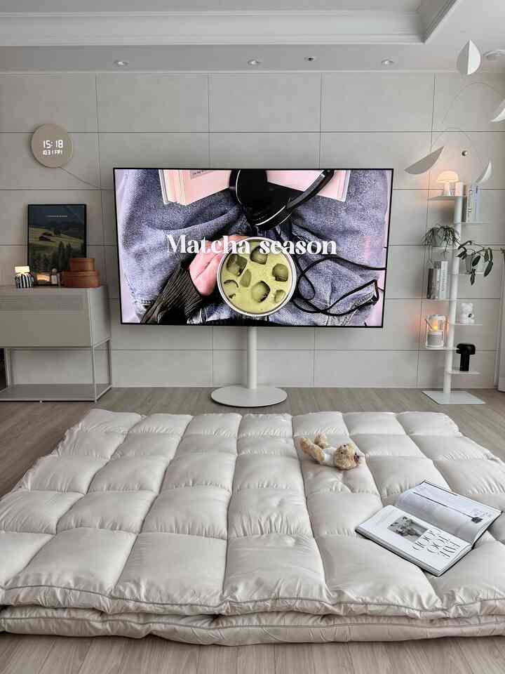 白い壁と大きなパディングベッドカバーが置かれたリビング、中央にテレビ台と壁照明があり、モダンな雰囲気のインテリア