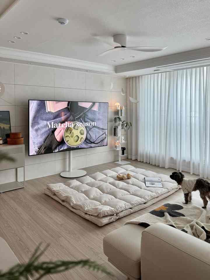 白と木目調のリビング、大型テレビスタンドと豆腐トッパーマットレス、ペットの犬がいるシンプルモダンな空間