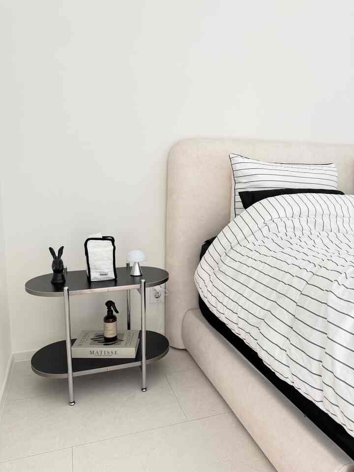 ミッドセンチュリーモダンの黒と白の寝室、黒のナイトテーブルとストライプの寝具が配置されたシンプルで機能的なインテリア