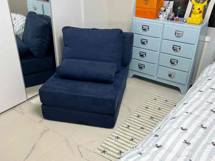 白い壁とネイビーカラーのソファが配置された、コンパクトでシンプルな寝室のインテリア