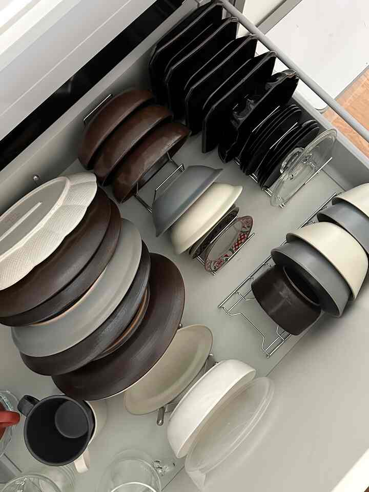 ブラウンとホワイトのトーンでまとめられたキッチンの引き出しに、様々な大きさと形の器や皿が整然と収納された印象的な空間