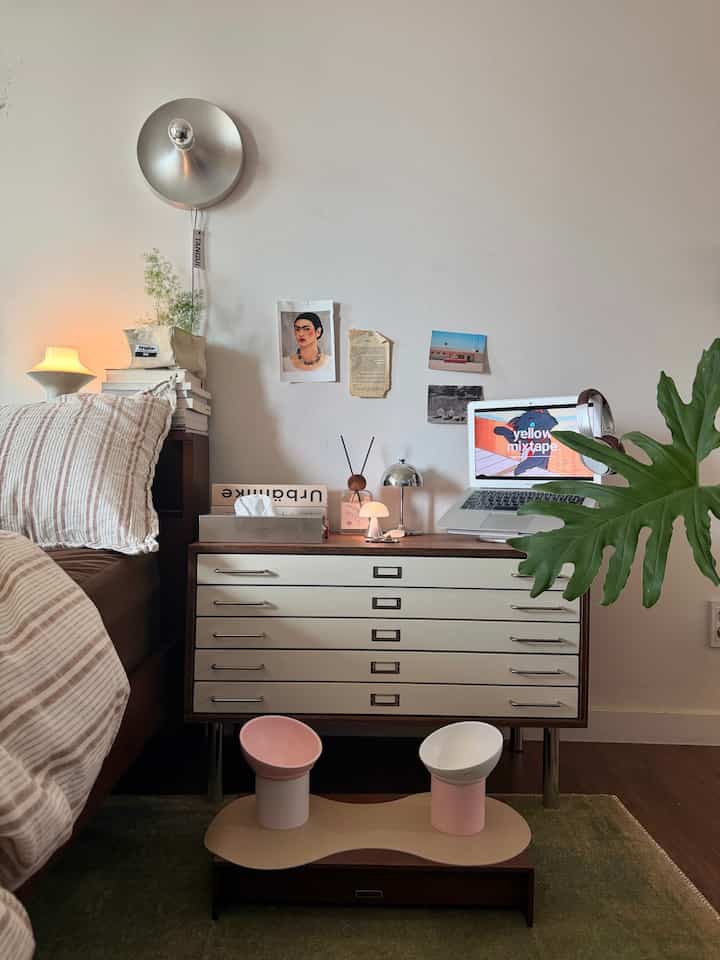 ナチュラルな色調の寝室、木製チェストとベッド、壁照明と2つのテーブルランプが配置された雰囲気のあるインテリア