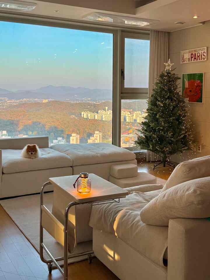 暖かいホワイトとウッドトーンのリビング、クリスマスツリーとソファが配置された居心地の良いシンプルな空間