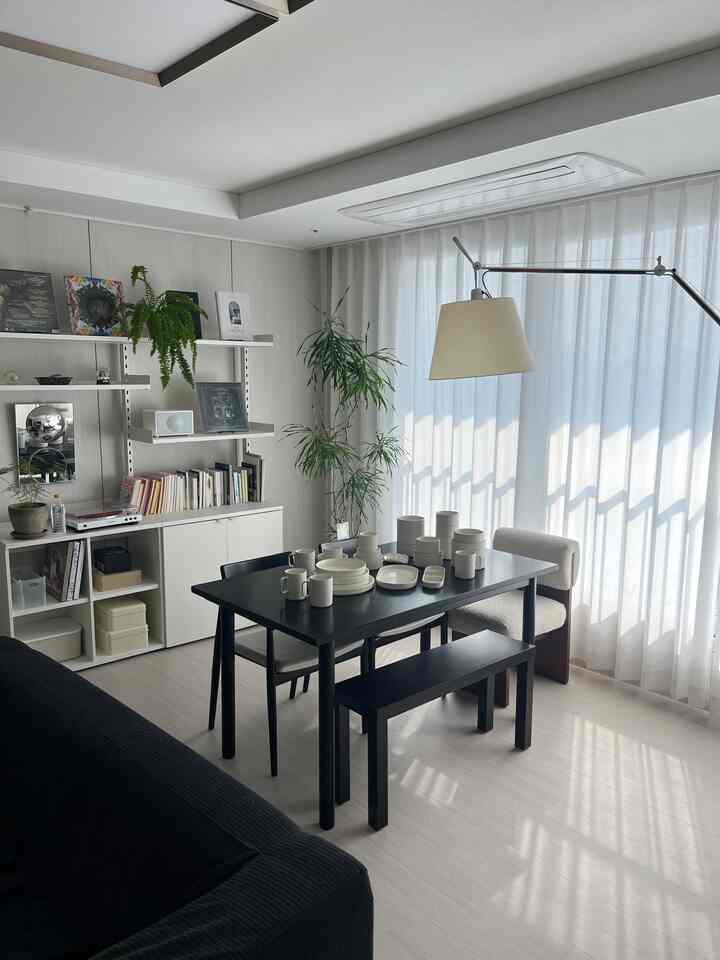 白と黒のトーンのリビング・ダイニングスペース、シンプルな黒のダイニングテーブルと白い食器セット、フロアランプと植物が調和した清潔感のあるインテリア