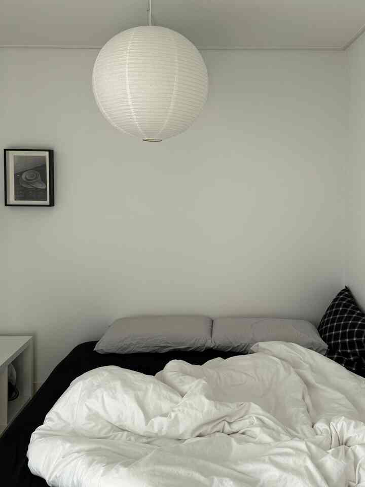モノトーンのグレーの壁、黒い寝具、グレーの枕、白いペンダントライトが配置されたシンプルな寝室