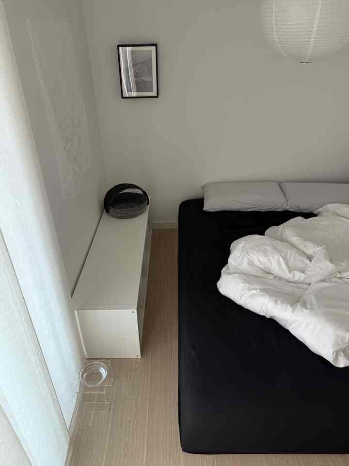 ホワイトとナチュラルウッド調のモダンな寝室、ブラックのベッドとすっきりとした収納棚が配置された落ち着いた空間