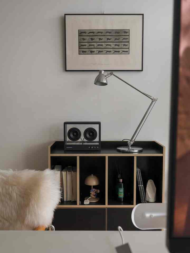白い壁と黒い本棚、透明なスピーカーとスタンドライトが配置されたシンプルな玄関スペース