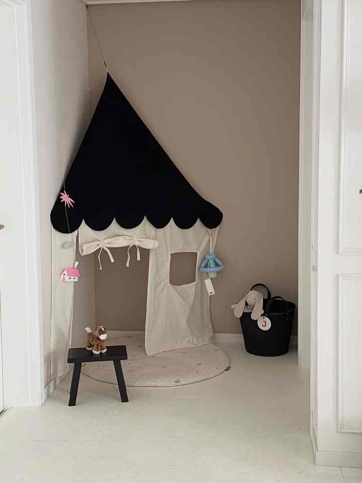 ベージュの壁と白い床、黒い屋根の子供用テントとおもちゃが置かれた子供部屋の遊び場