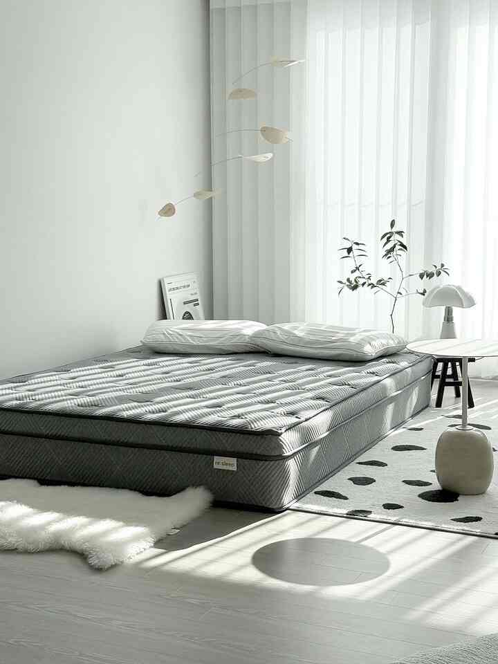 白とグレーのトーンの寝室、ロータイプベッドとラグ、自然光と観葉植物が調和したモダンでナチュラルなインテリア