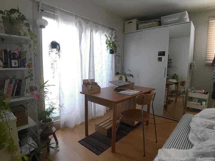 明るい白いカーテンとナチュラルウッド家具が配置された8坪のワンルーム、一人用の作業スペースが印象的なインテリア