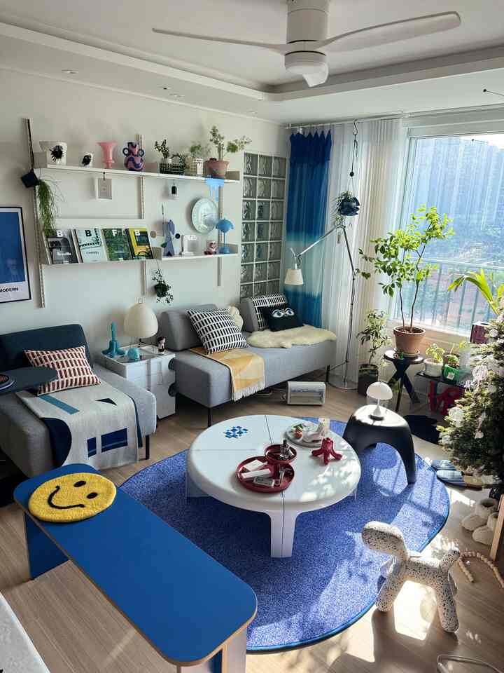 青色が際立つリビング、グレーのソファと丸いテーブル、多様な植物が配置された明るく落ち着いた空間