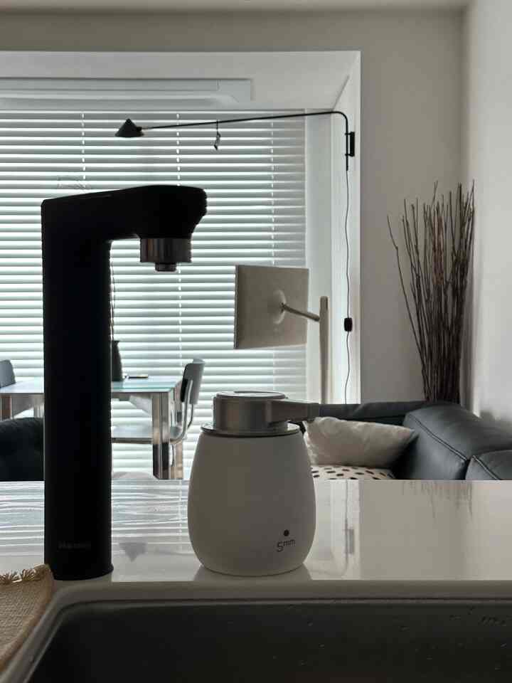 白と黒のトーンが特徴のキッチンとリビング、ブラインドとソファが配置されたミニマルで清潔感のあるインテリア