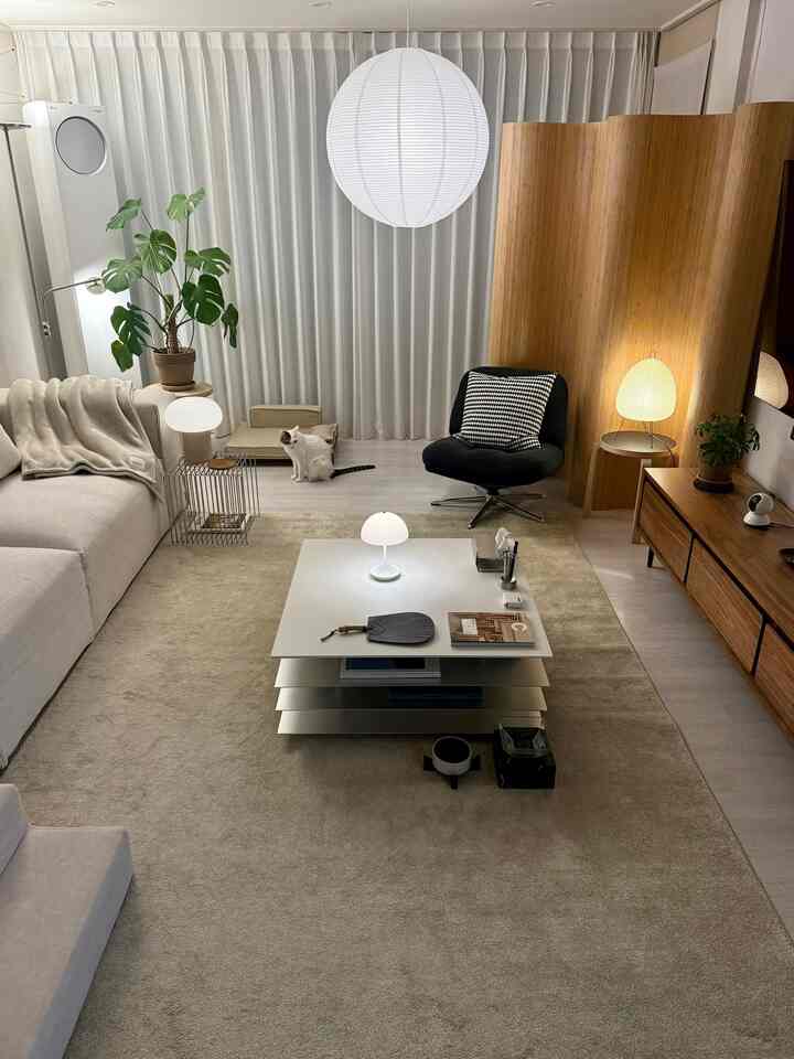 白とオートミールベージュの色調のリビング、ベージュのソファとブランケット、猫、自然な木製家具と照明が調和したシンプルで雰囲気のあるインテリア