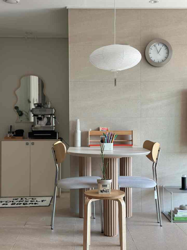 ベージュの壁と明るい木製家具が調和したキッチンのナチュラルな空間、丸テーブルと椅子、コーヒーマシンが配置されたおうちカフェの雰囲気