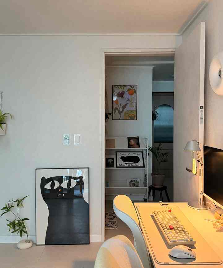 明るいホワイトトーンの書斎、白いデスクと椅子が配置され、黒い猫のポスターと植物が調和した雰囲気のあるインテリア