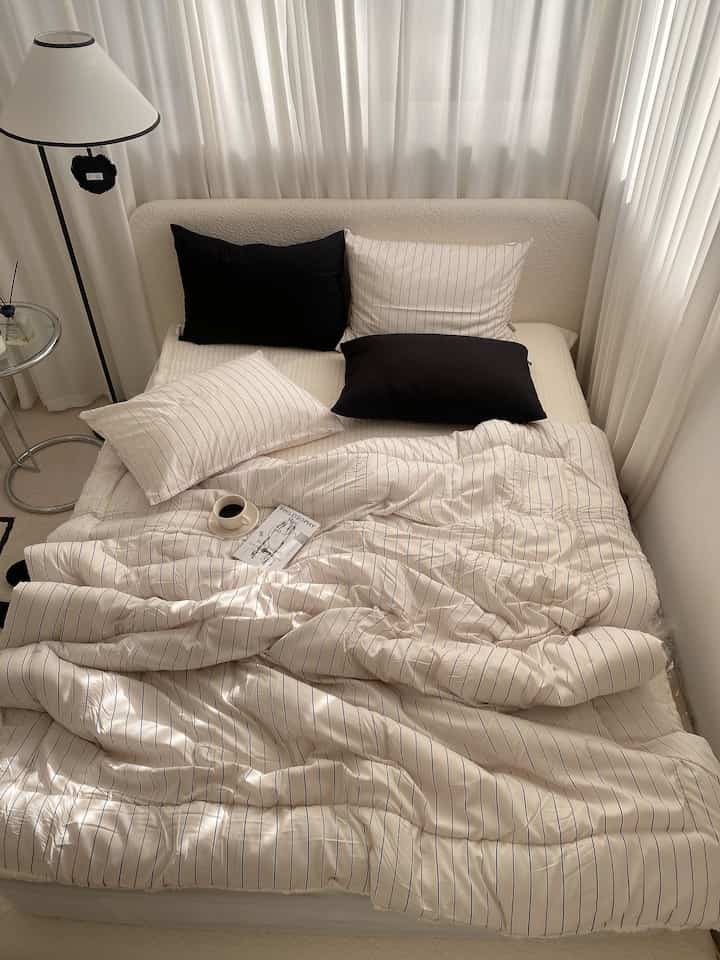 白と黒の調和が取れた寝室、ストライプの寝具とフロアランプが配置された温かみのある空間