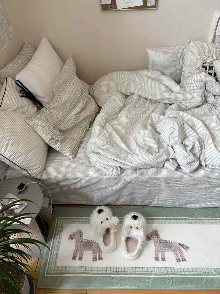 白とベージュのトーンが調和したナチュラルな印象の寝室。中央に複数の枕と掛け布団が配置された居心地の良いベッド。