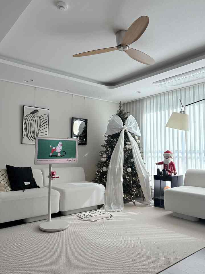 白を基調としたリビング、巨大な白いリボンのクリスマスツリー、ソファとフロアランプが配されたモダンで清潔感のあるインテリア
