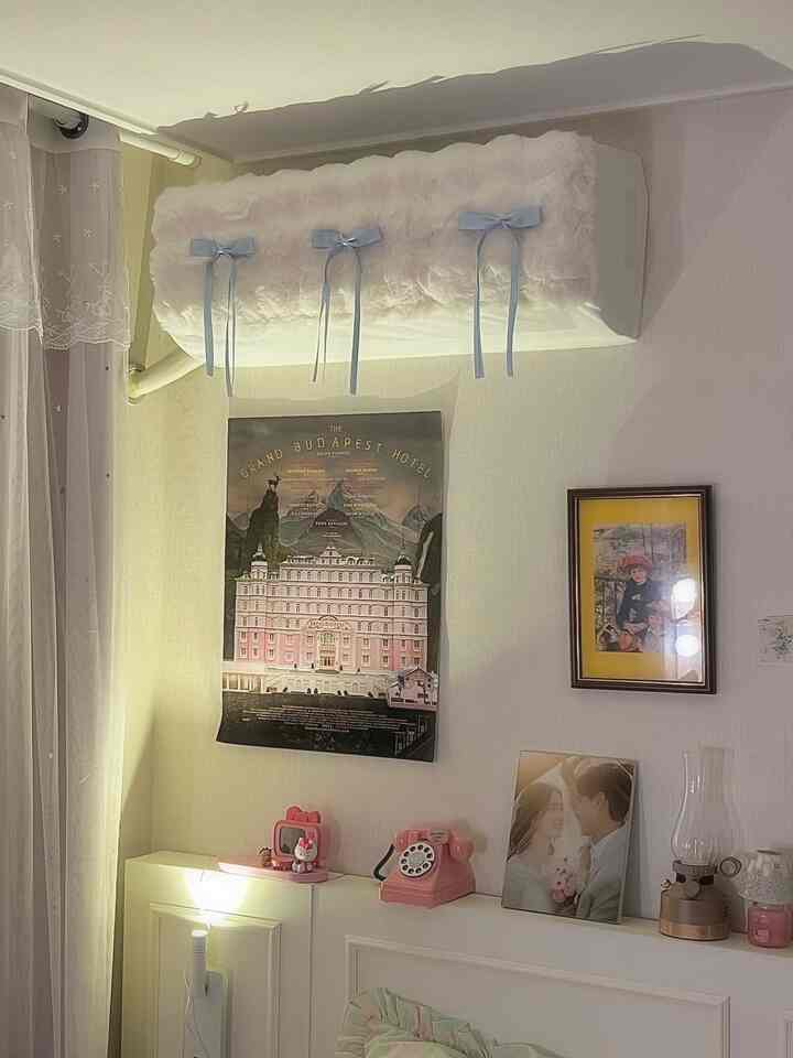 ホワイトトーンのリビングの壁にヴィンテージポスターとピンクの小物が配置された雰囲気ある空間