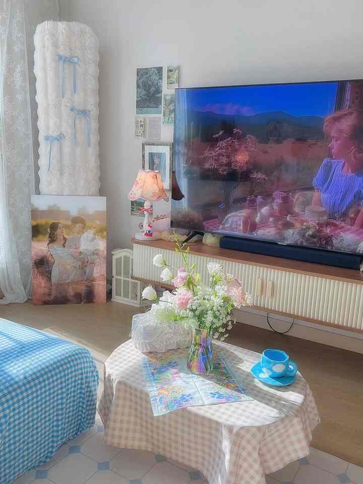 パステルトーンとスカイブルーのアクセントが映えるリビング、エアコンカバーとレースカーテン、花瓶の置かれた温かみのあるテーブルのある空間