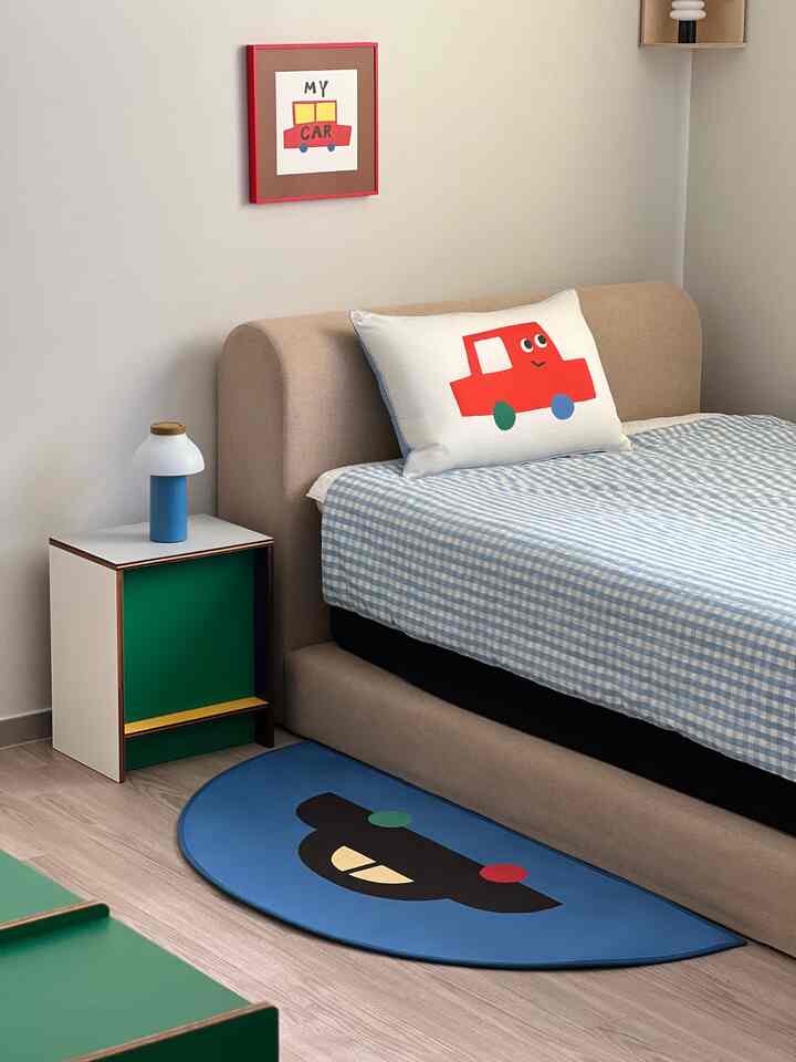 ブルーとベージュの色調の子供部屋、車のイラスト入りの枕とラグが配置されたかわいらしい空間