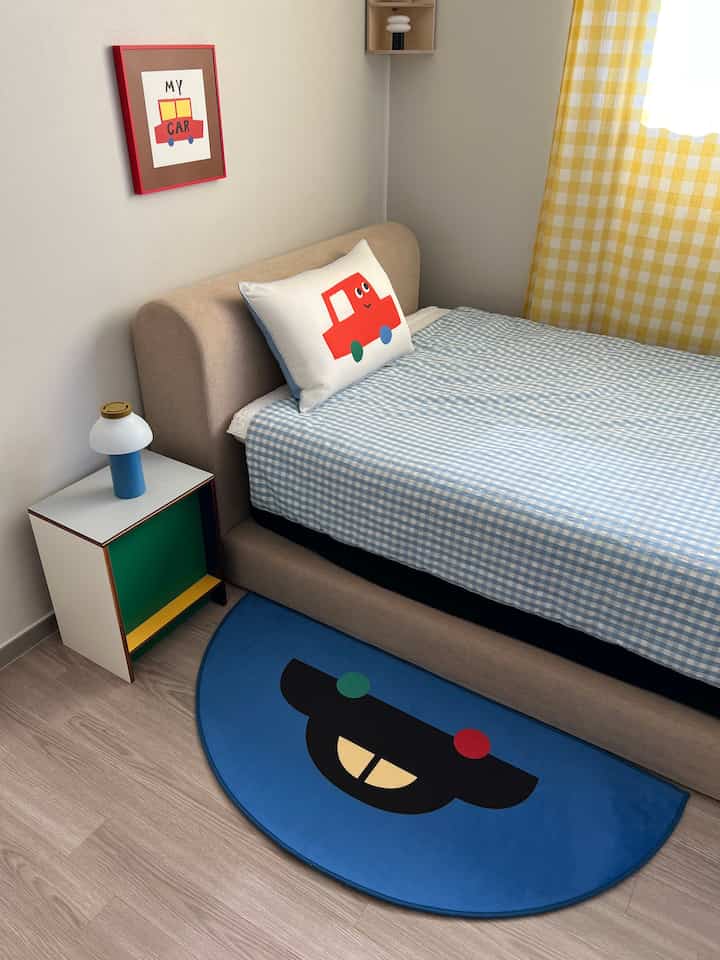 ブルーとベージュの色調の子供部屋、赤い車のクッションとポスターが配された温かみのある寝室