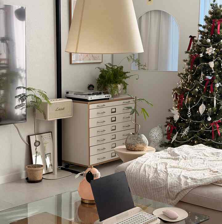ホワイトとベージュのトーンのリビング、ソファベッドとドレッサー、クリスマスツリーが配置された居心地の良いホームオフィス空間