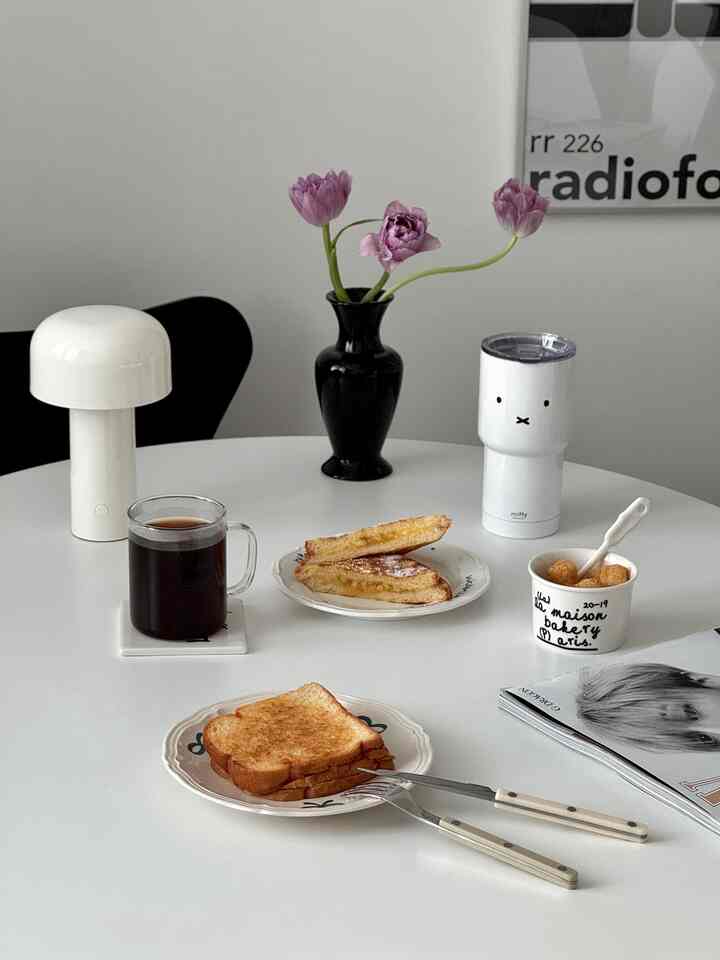 ホワイトトーンのダイニングテーブルにモダンなテーブルランプと花瓶、トーストとコーヒーが置かれたおうちカフェの雰囲気のあるインテリア