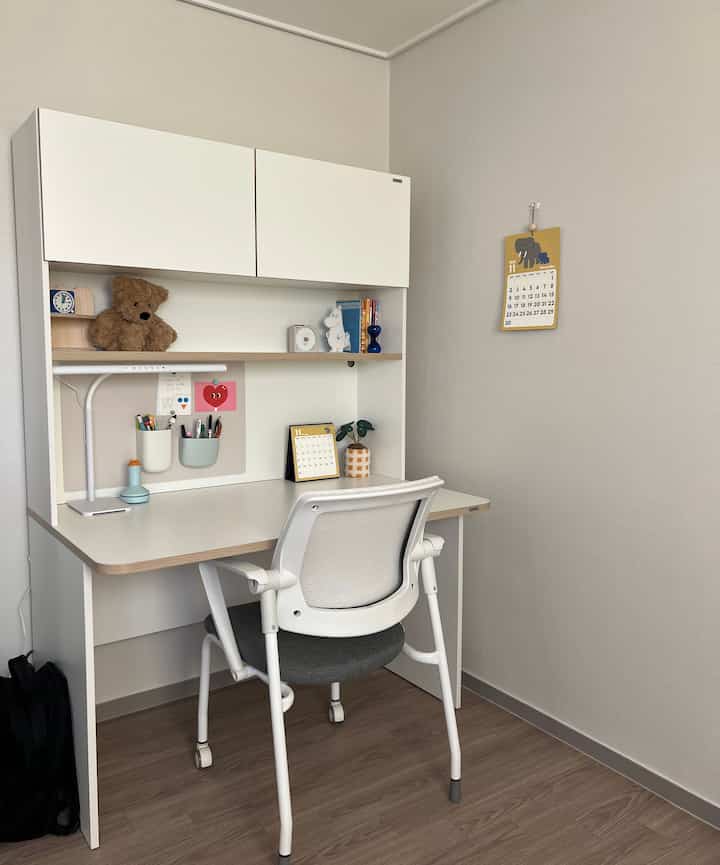白と茶色のトーンの子供部屋の学習スペース、シンプルで整頓された机と壁掛けカレンダーが配置された雰囲気のあるインテリア