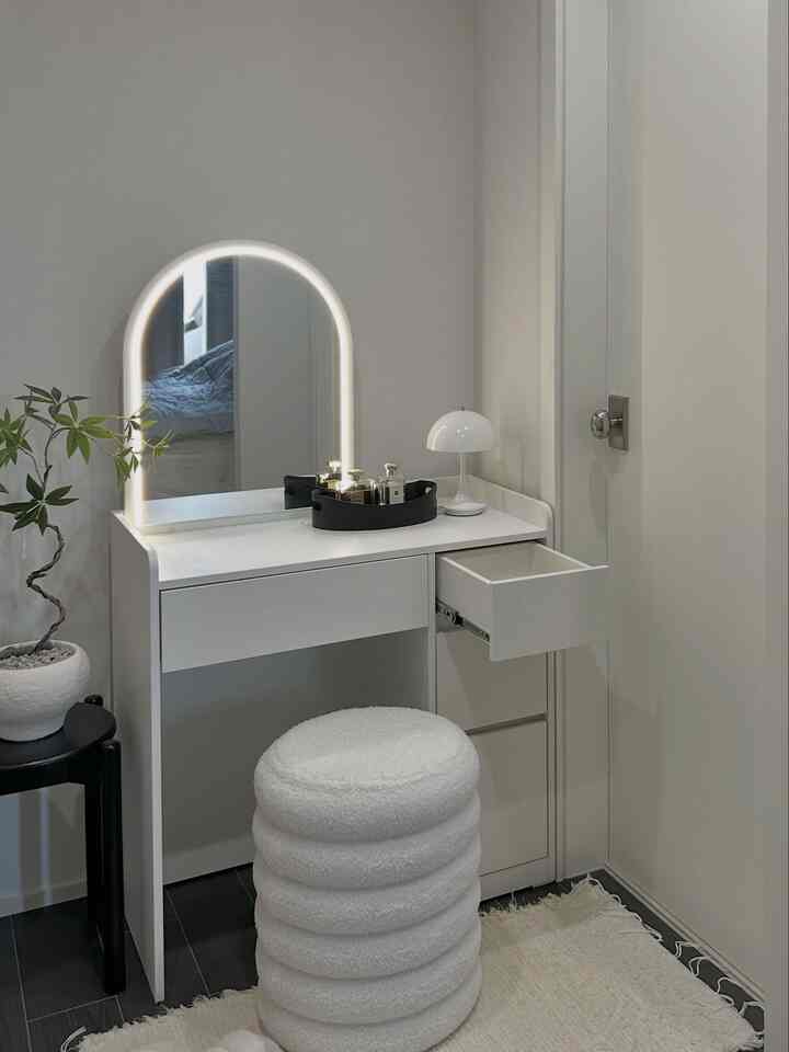 ホワイトトーンの化粧台とブークレスツール、照明付きのアーチミラーが配置されたミニマルでシンプルな空間