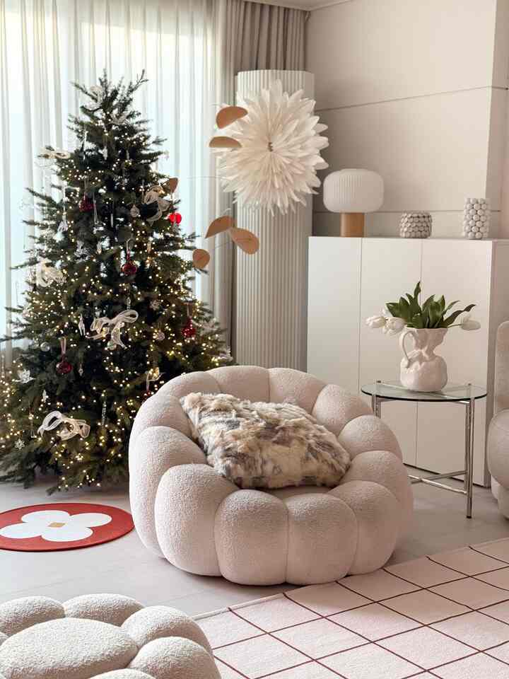 ナチュラルモダンなトーンのリビング、クリスマスツリーと丸いソファ、ファークッションとサイドテーブルが配置された雰囲気のある空間