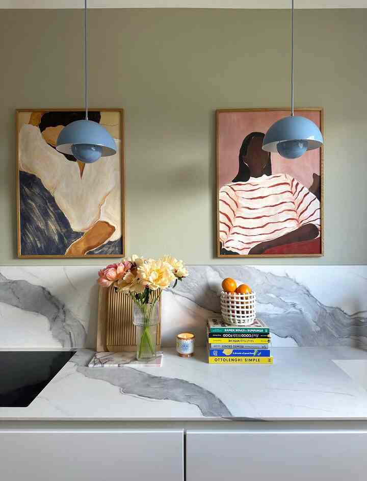 Modern kitchen with soft sage walls and marble countertop, featuring two pendant lights and abstract wall art creating an inviting ambiance