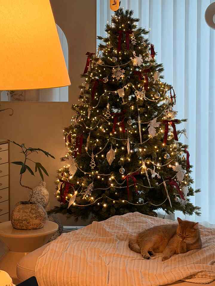暖かいホワイトトーンのリビング、印象的な大型クリスマスツリーとフロアランプが配置された雰囲気のあるインテリア