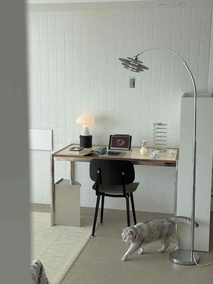 白とグレーのトーンのホームオフィス、クロム製のデスクと照明、猫がゆったり歩く雰囲気のあるインテリア