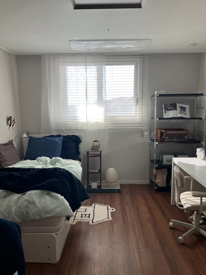 ホワイトとウッドトーンが調和するワンルーム寝室、ベッドとデスクを配置した清潔感のある居心地の良い空間