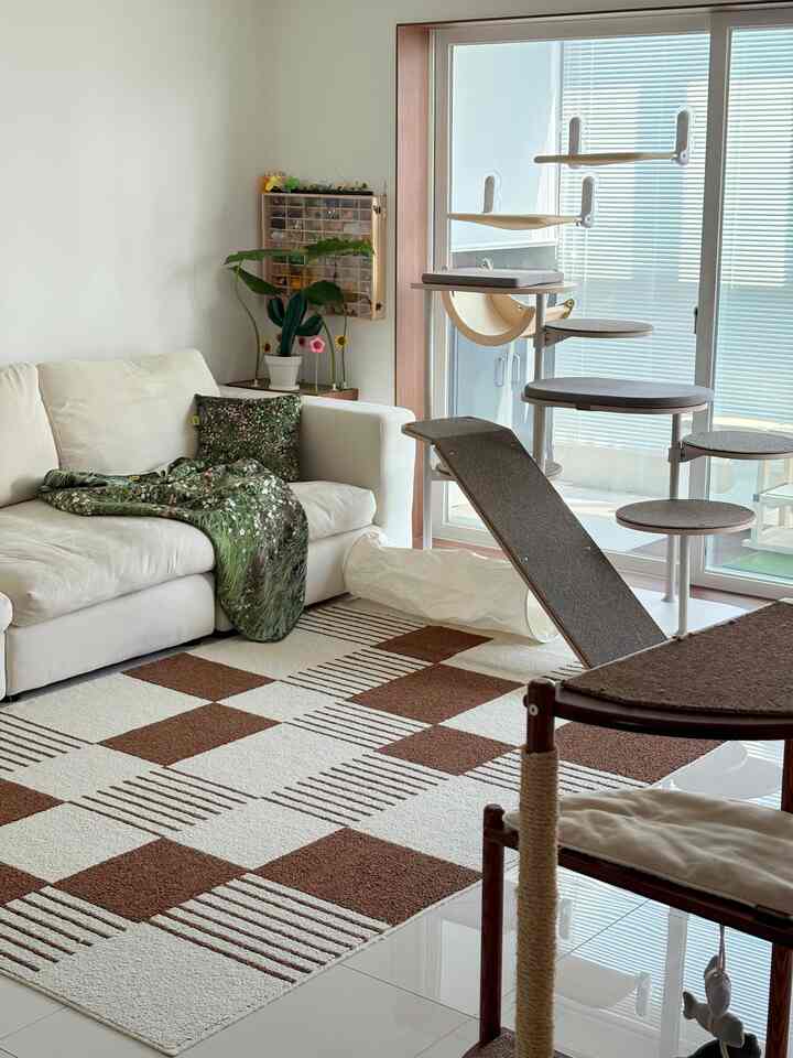 白と茶色の色調のリビング、猫のキャットタワーと白いソファが配置された落ち着いた空間