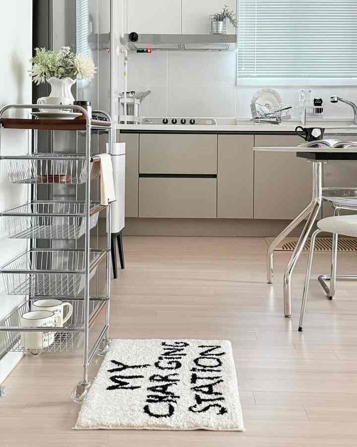 ホワイトとベージュのトーンのキッチン、整理されたキッチンワゴンときれいなブラインドが配置されたモダンな空間