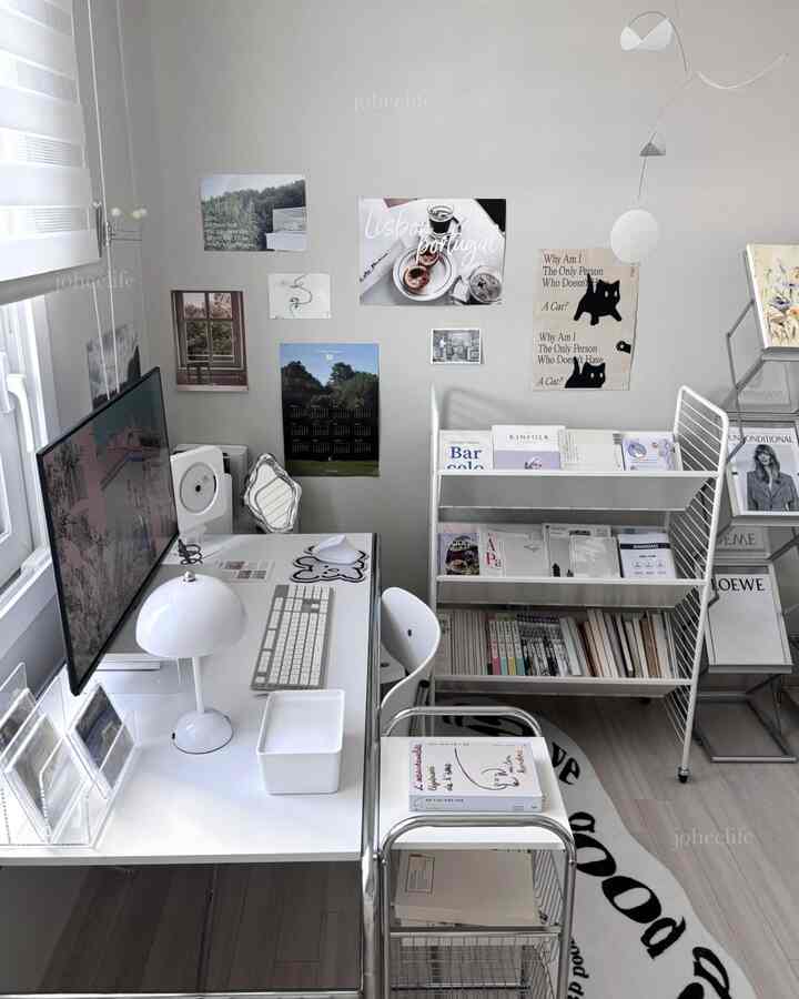 ホワイトとシルバーのトーンが映えるモダンな書斎、整頓されたデスクと棚、壁には多彩なポスターとモビールが配置された落ち着いた作業空間