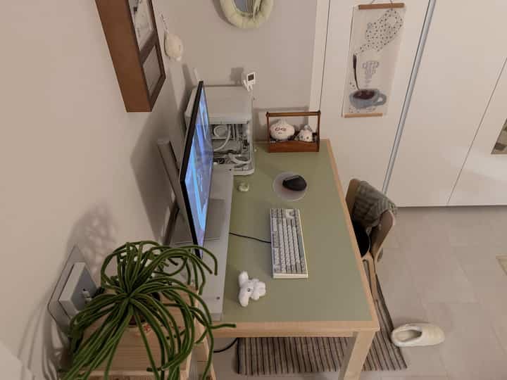 明るい白い壁と木目調家具が調和するコンパクトなホームオフィス空間、モニターとキーボードが置かれたデスクが在宅勤務の環境を作り出す