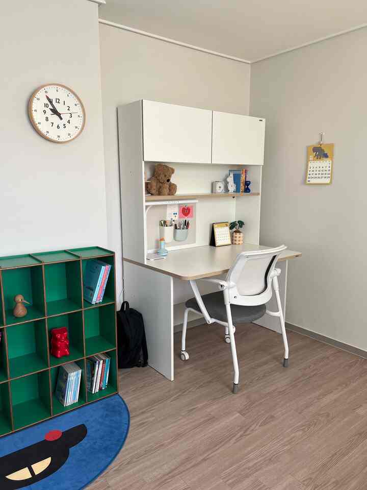 白と緑のトーンの子供部屋、落ち着いた白いデスクと緑の本棚、かわいい壁掛けカレンダーが配置されたシンプルな勉強空間