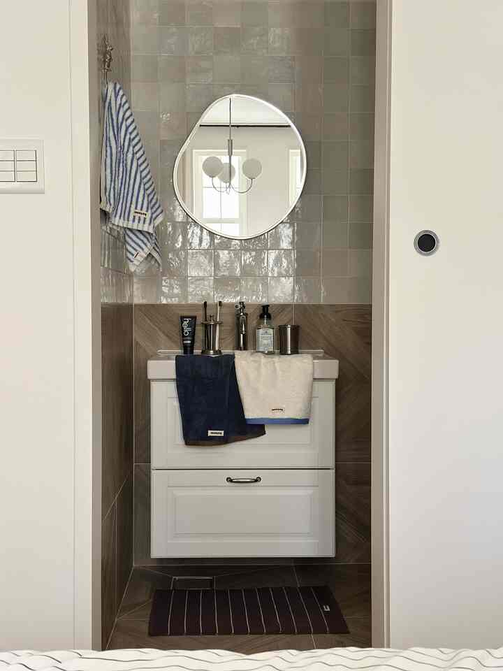 ホワイトとブラウンの色調のバスルーム、丸い鏡とストライプのタオルが配置された印象的な空間